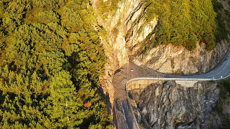 Auf dem Bild ist eine Kurve der Hantennjochstraße zu sehen, auf die eine Mure abgerutscht ist.