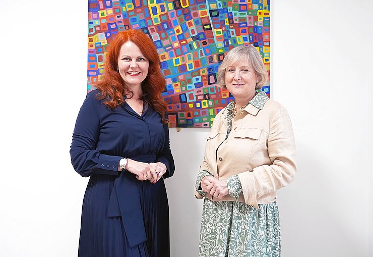 LRin Cornelia Hagele zusammen mit der ausgezeichneten Gabriele Lehner vor einem Gemälde mit bunten Vierecken.