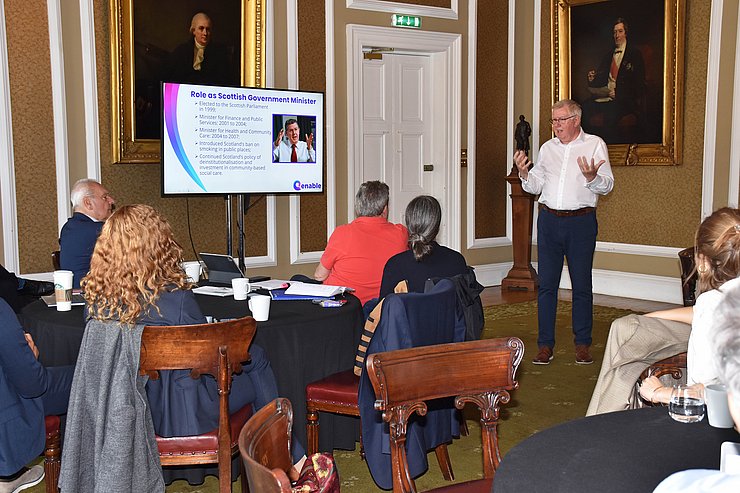 altehrwürdiger Raum, Personen sitzen an Tischen, vorne spricht Kerr