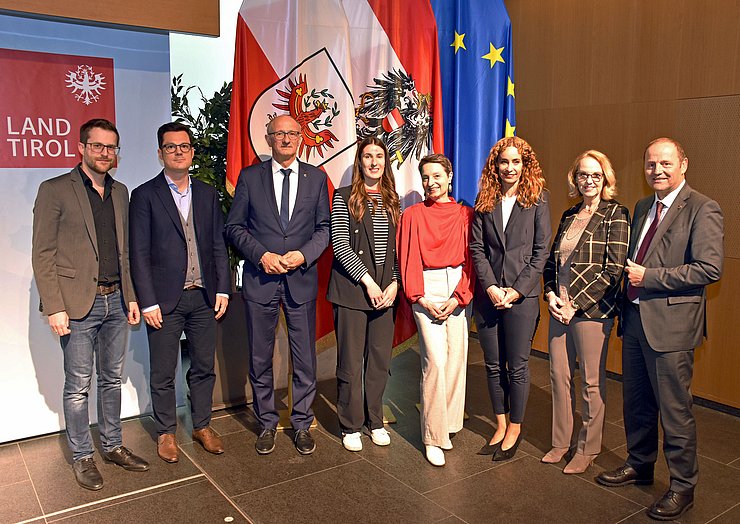 © Land Tirol/Neuner Mehrere Menschen stehen im Großen Saal des Landhause vor drei Fahnen.
