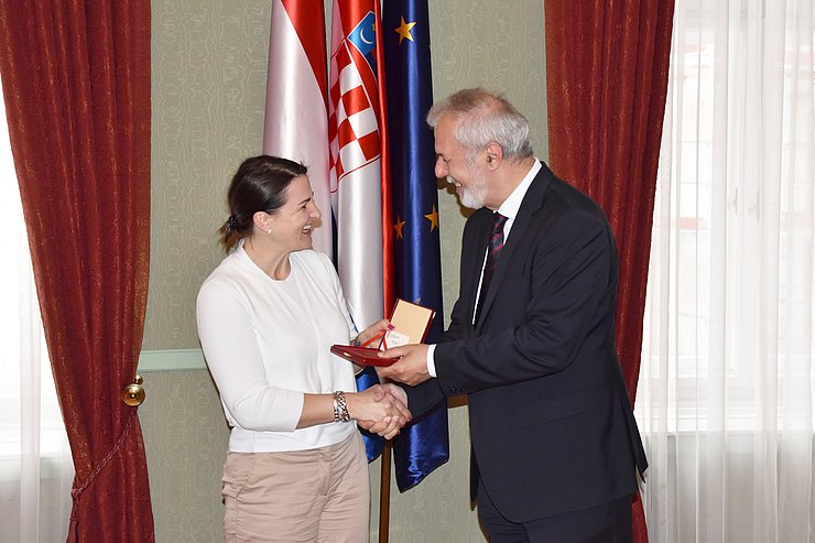 © Land Tirol/Pölzl Sanader übergibt Mair eine Schachtel; sie schütteln einander die Hand und lachen