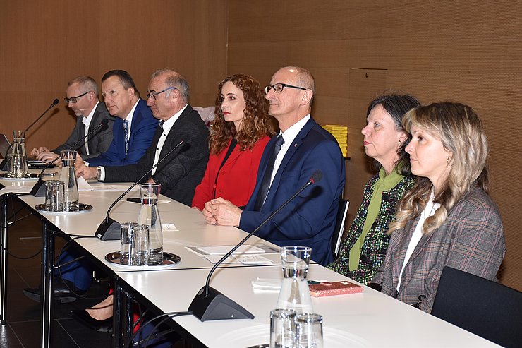 Personen sitzen nebeneinander an Redepult