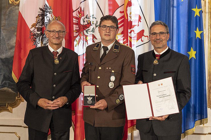 © Land Tirol/Die Fotografen links LH Mattle, in der Mitte Herr Saxer und rechts LH Kompatscher, halten Medaille und Verdiensturkunde