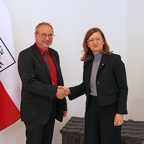 Zwei Menschen posieren neben einer Flagge.