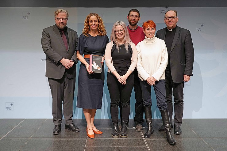 © Land Tirol/Dorfmann Personen stehen nebeneinander, LRin hält Buch in Händen