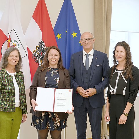 Personen stehen vor Fahnen, Malaun hält Dekret