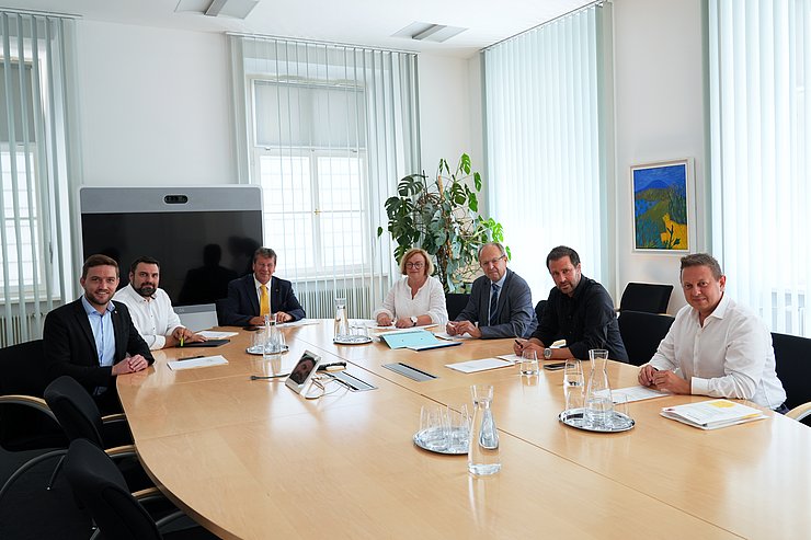 © Land Tirol Die Mitglieder des Wohnbauförderungskuratoriums sitzen bei ihrer jüngsten Sitzung im Landhaus in Innsbruck um einen ovalen Tisch schauen für das Gruppenfoto in die Kamera