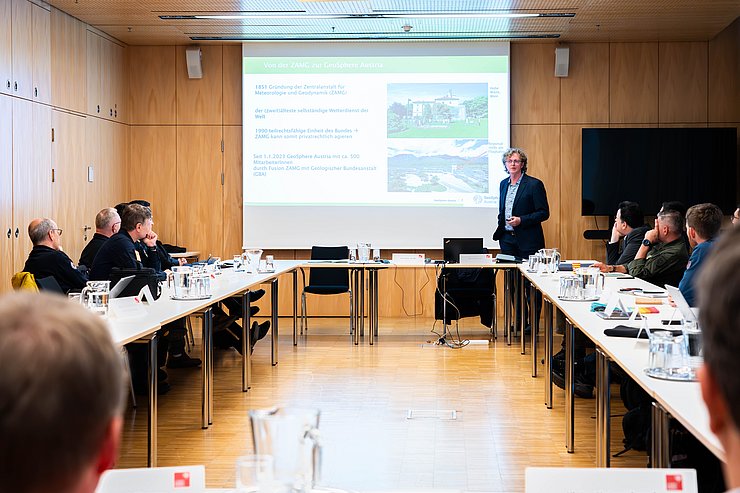 Bauer vor Publikum stehend und sprechend; Leinwand mit Powerpoint-Präsentation