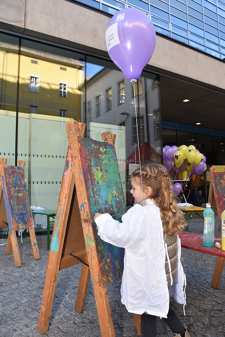 Kind malt auf einer Leinwand, die auf einer Staffelei ist.