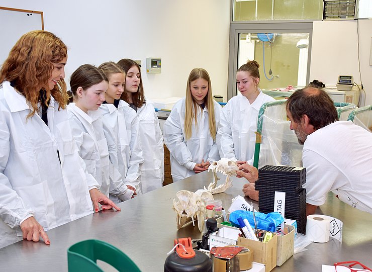 Mehrere Mädchen und eine Frau stehen vor einem Tisch mit Schädelknochen.