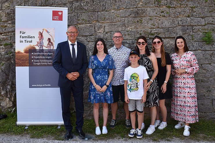 LH Mattle und LRin Mair mit fünfköpfiger Familie vor Mauer und Land-Tirol-Rollup