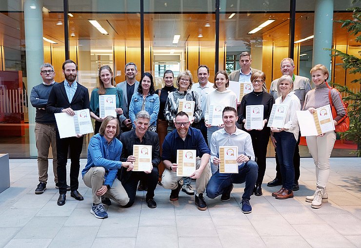 Gruppenaufnahme vor einer Glasfassade, bei der die Männer und Frauen Urkunden in der Hand halten. 