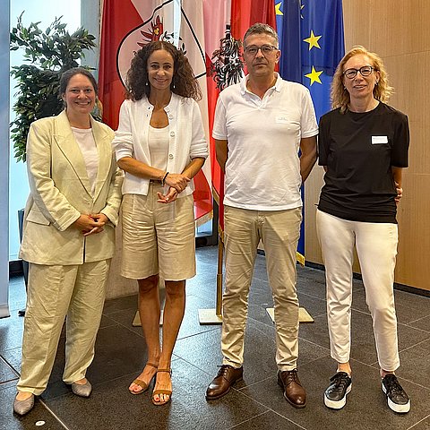 Gruppenfoto, Personen nebeneinander im Großen Saal des Landhauses, vor Fahnen