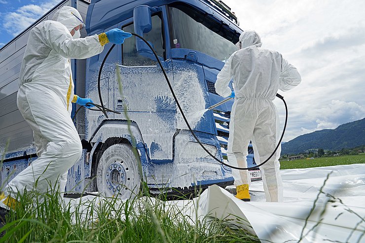 Personen in weißer Schutzausrüstung besprühen LKW mit weißem Schaum