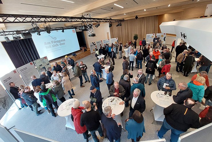 Übersichtsfoto der Veranstaltung: Zahlreiche Personen in Saal stehen um Tische oder schauen sich Plakate an Stehwänden an 