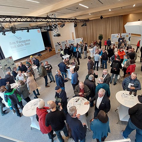 Übersichtsfoto der Veranstaltung: Zahlreiche Personen in Saal stehen um Tische oder schauen sich Plakate an Stehwänden an 