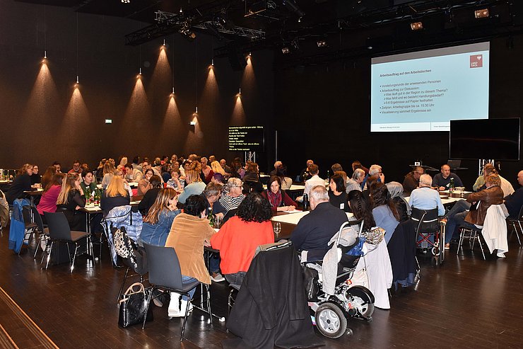 Saal mit Tischen und vielen Leuten