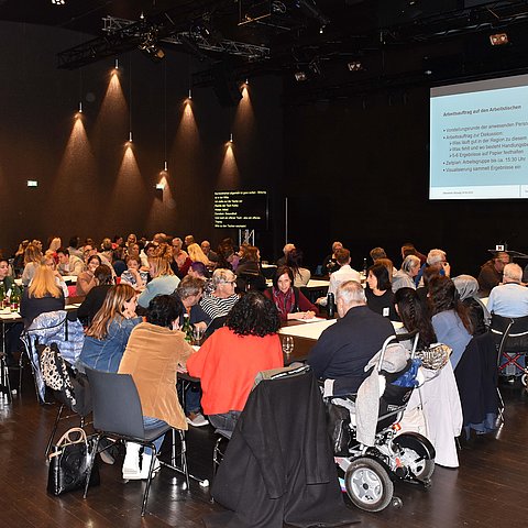 Saal mit Tischen und vielen Leuten