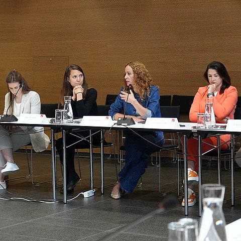 LRin sitzt mit weiteren Personen an länglichem Tisch, gestikuliert