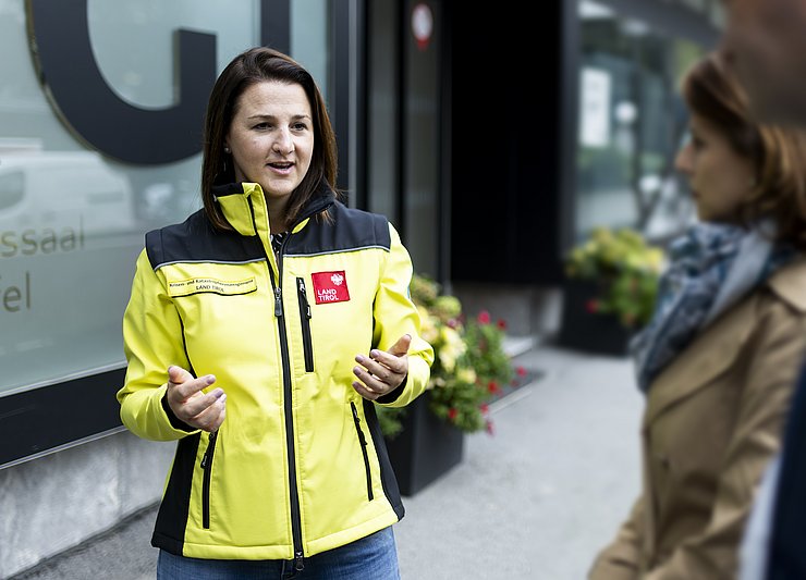 © Land Tirol Sicherheitslandesrätin Astrid Mair in gelber Einsatzjacke im Gespräch mit zwei weiteren Personen