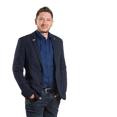 Ein Mann steht aufrecht und schaut direkt in die Kamera.