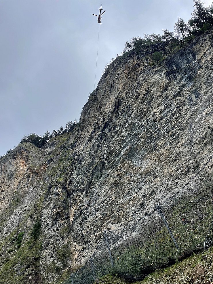 © Land Tirol Eine Felswand mit einem Helikopter der daneben fliegt.