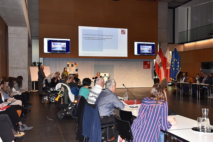 Saal mit Personen - vorne wird auf Leinwand Präsentation gezeigt