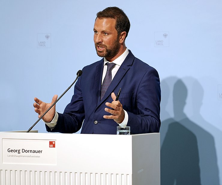 © Land Tirol/Neuner LHStv Georg Dornauer steht hinter einem weißen Pult und spricht zu den JournalistInnen.