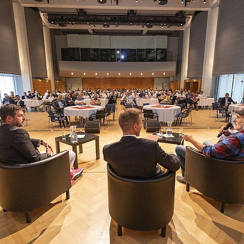 Saalüberblick: Redner auf Podium von hinten und Publikum von vorne
