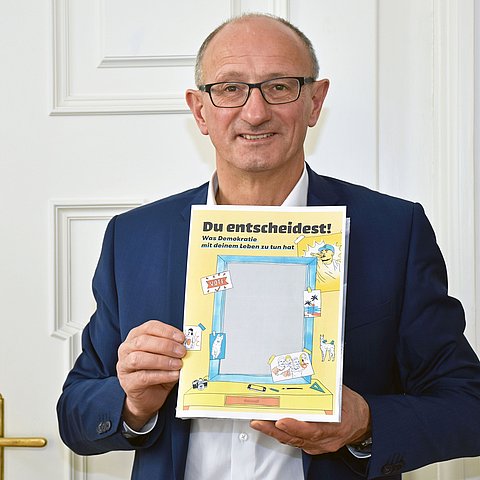 Jugendlandesrat Anton Mattle mit dem Deckblatt der Demokratiebroschüre „Du entscheidest!“ der österreichischen Jugendinfos.