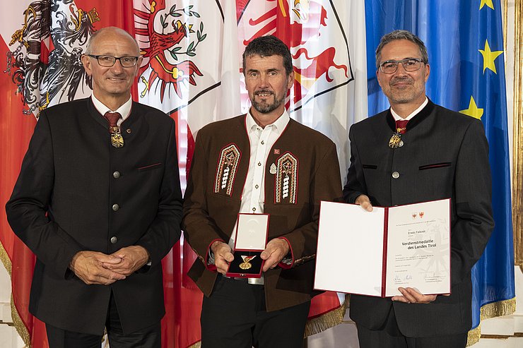 © Land Tirol/Die Fotografen links LH Mattle, in der Mitte Herr Falkner und rechts LH Kompatscher, halten Medaille und Verdiensturkunde