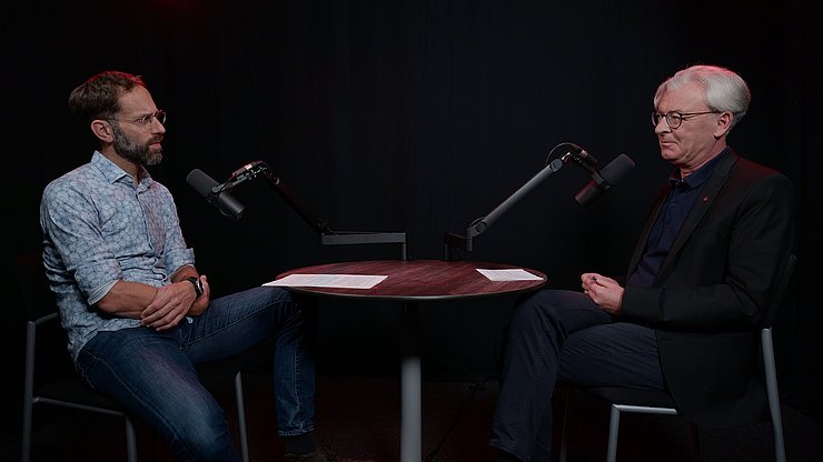 Personen sitzen vor Mikros an Tisch