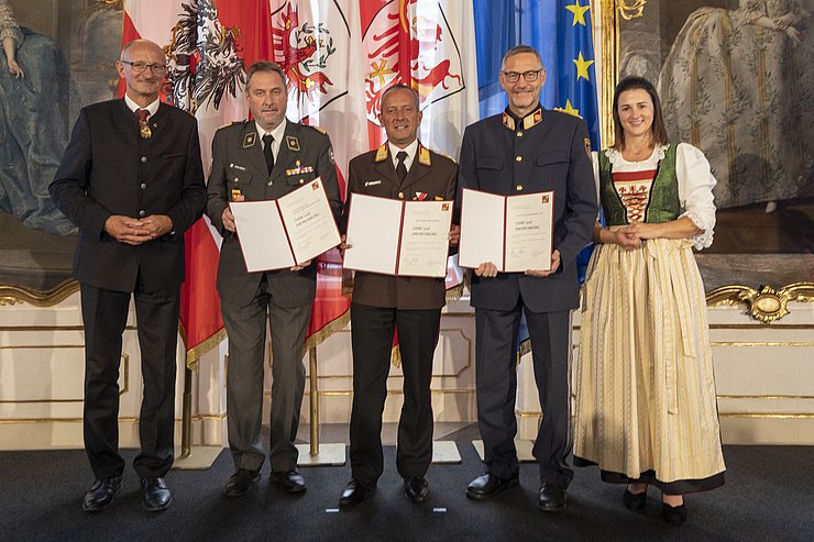 © Land Tirol/Die Fotografen links LH Mattle, in der Mitte die drei Vertreter der Einsatzorganisationen, halten Urkunden, rechts LRin Mair