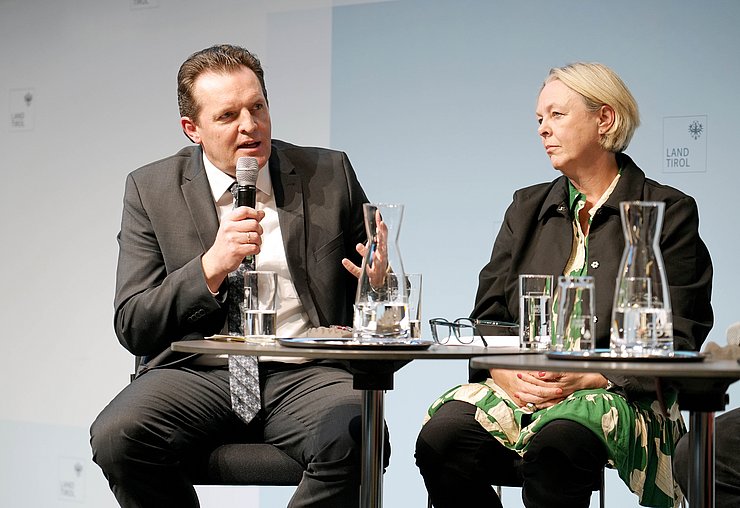 Ein Mann redet in ein Mikrofon und gestikuliert mit der linken Hand. 