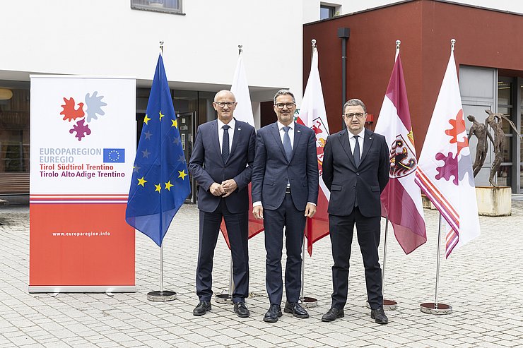 Personen stehen nebeneinander, vor Fahnen und Euregio Roll-up