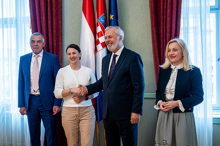 © Land Tirol/Christanell Gruppenfoto: Mair und Sanader in der Mitte, schütteln einander die Hand; im Hintergrund Fahnen von Österreich, Kroatien und der EU