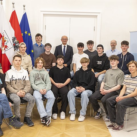 Eine Gruppe von Schülern sitzt bzw. steht in einem Halbkreis, in der Mitte befindet sich LH Anton Mattle.