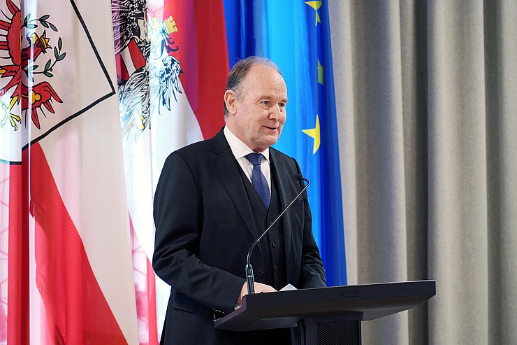 Ein Mann steht an einem Rednerpult vor Fahnen.