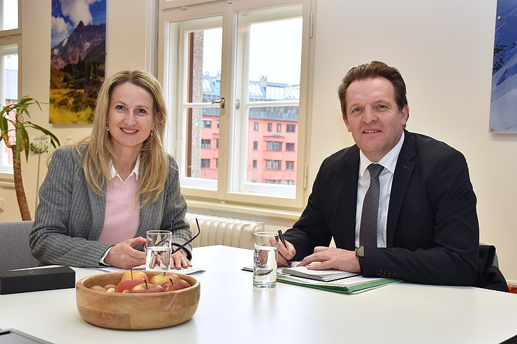zwei Personen sitzen am Tisch, Blick in die Kamera
