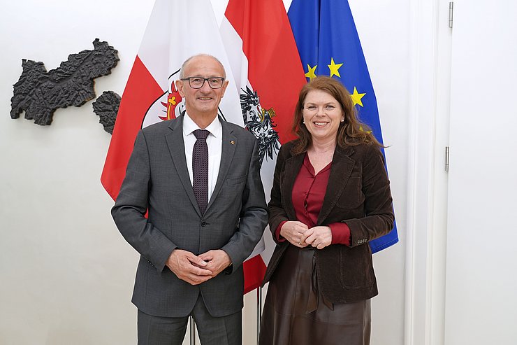 Zwei Menschen posieren vor mehreren Flaggen.