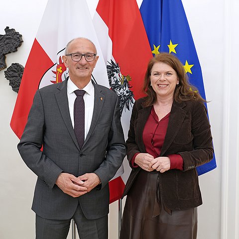 Zwei Menschen posieren vor mehreren Flaggen.