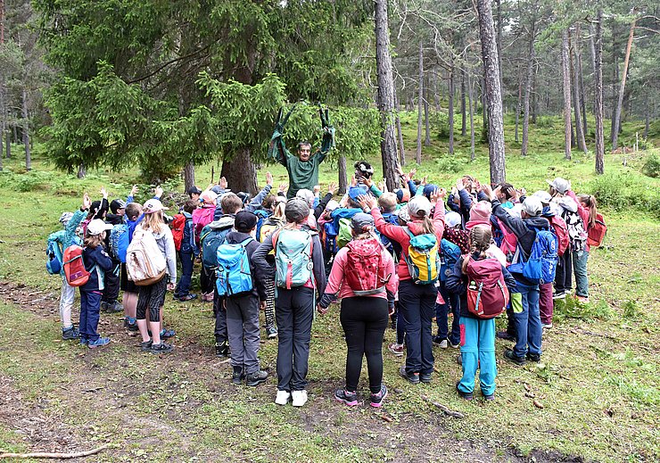 © Land Tirol/Hörmann Eine große Gruppe an Kindern stehen im Wald und beobachten ein Theaterspiel.