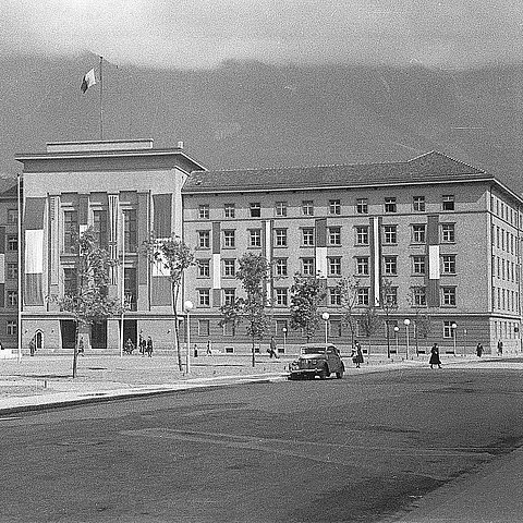 Eine Schwarz-Weiß-Aufnahme eines im NS-Stil errichteten Verwaltungsgebäudes, das mit den Fahnen der französischen Besatzungsmacht sowie Österreichs beflaggt ist.