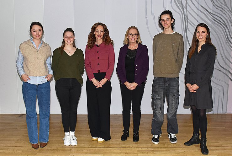 Gruppenfoto: Personen stehen nebeneinander aufgereiht vor grauer Wand