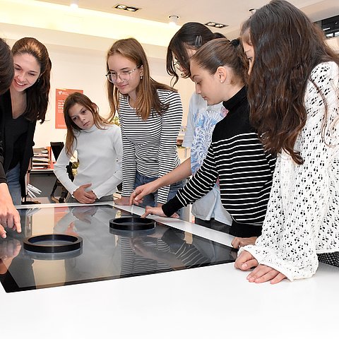 Eine Frau zeigt auf einen Bildschirm am Tisch.