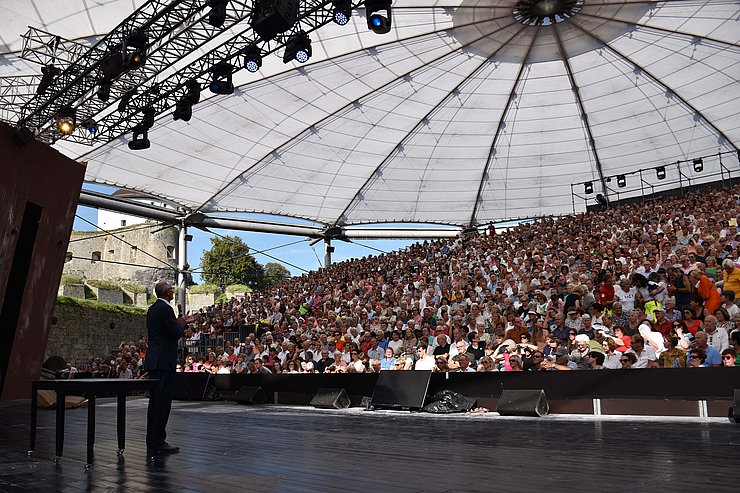 LH Mattle hält Ansprache auf Bühne, Bild von hinten auf Menschenmenge auf Tribüne
