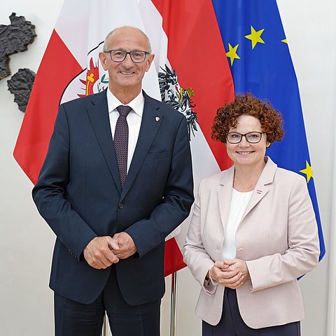 Zwei Menschen posieren vor mehreren Flaggen.