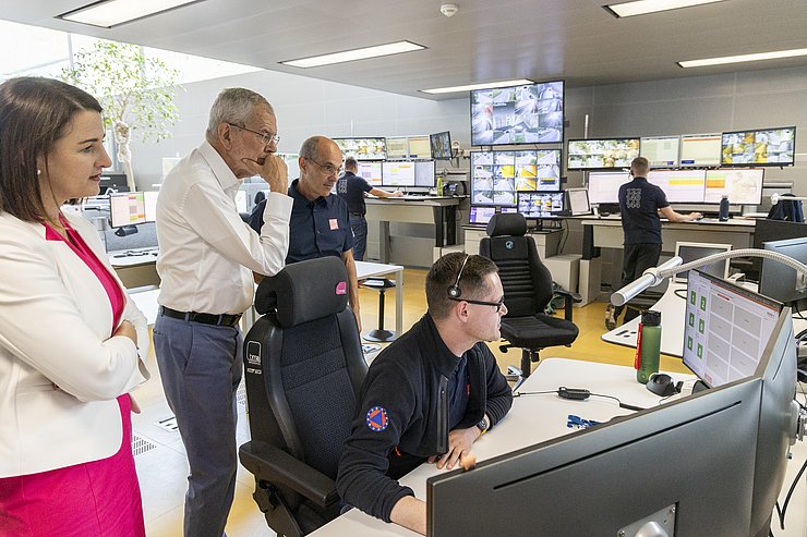 Van der Bellen steht bei Schreibtisch mit Mitarbeiter der Leitstelle, der auf Bildschirme vor sich schaut
