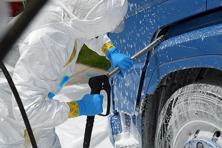 Person in weißer Schutzausrüstung besprüht LKW mit weißem Schaum