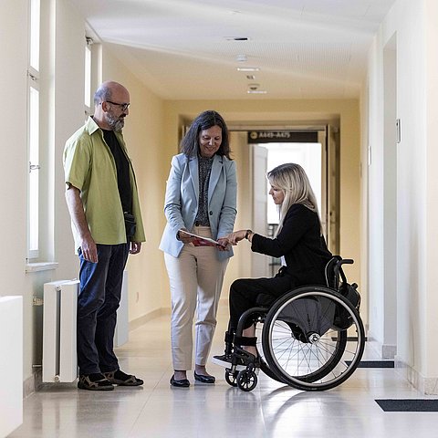 drei Personen in Gang, eine Person im Rollstuhl